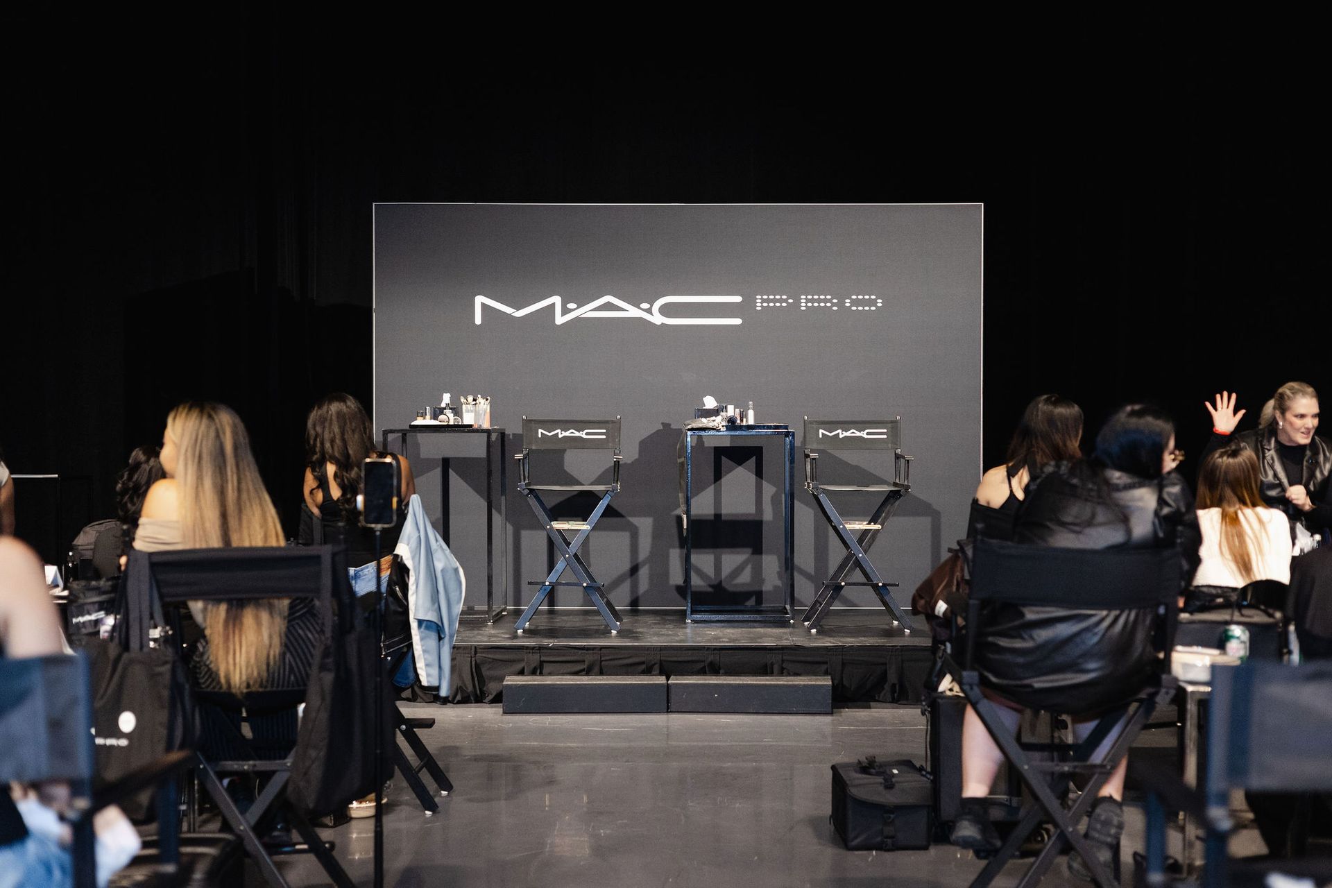 MAC Pro makeup event: Attendees seated, watching a demonstration stage with products.