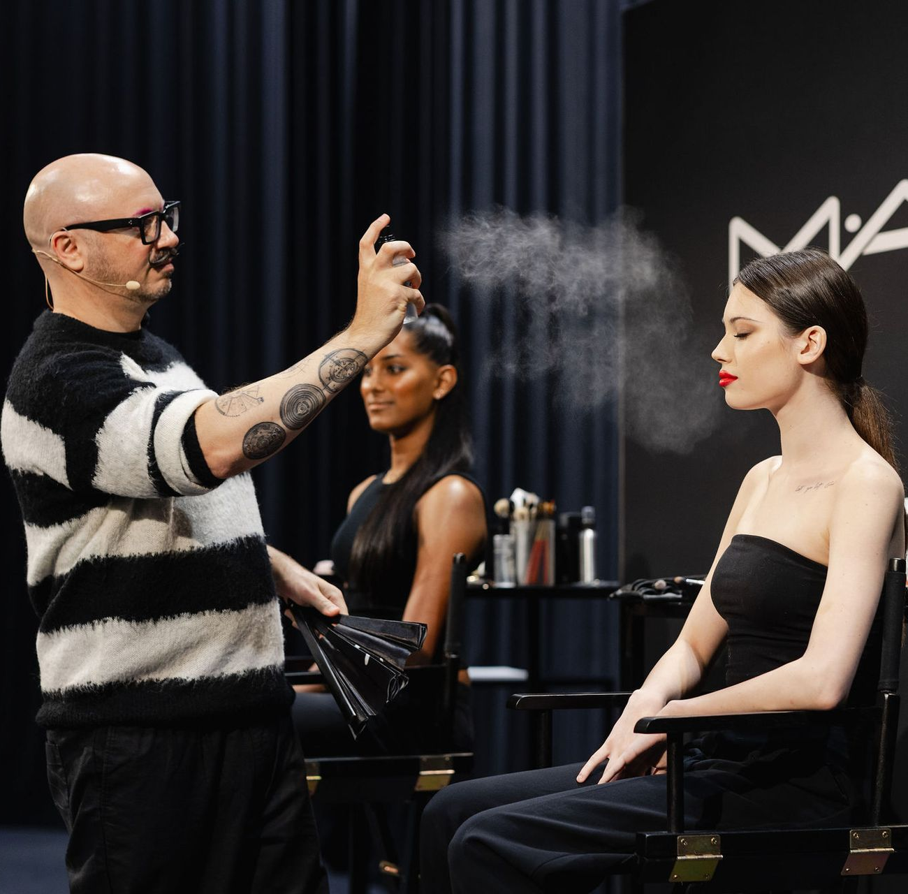 Hairstylist spraying hair product on seated client in a salon-like studio