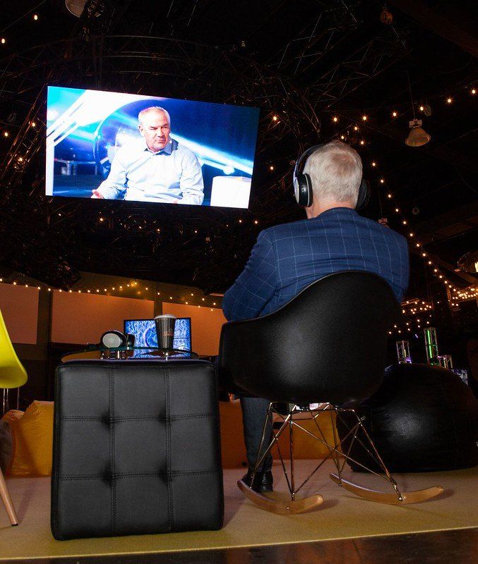 A man wearing headphones sits in a chair watching a television