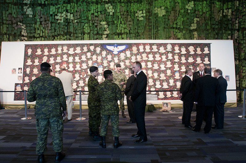 A group of men in military uniforms are standing in front of a wall with pictures on it.