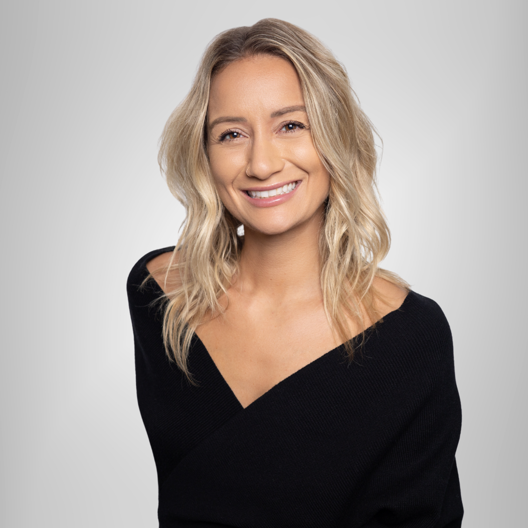 Smiling blonde woman in a black top against a light gray background