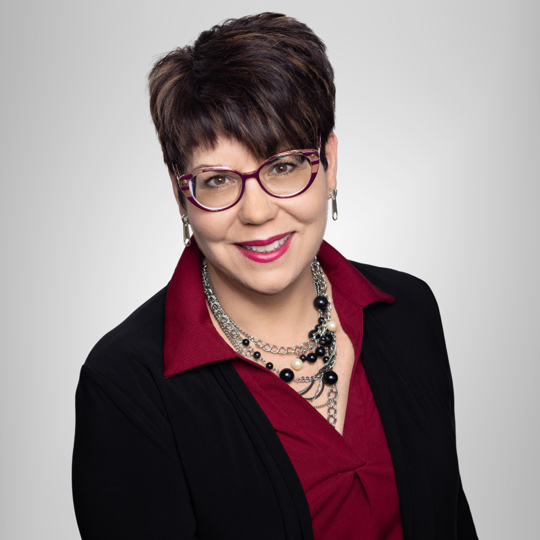 Portrait of a smiling woman with short dark hair, glasses, and red blouse under a black jacket