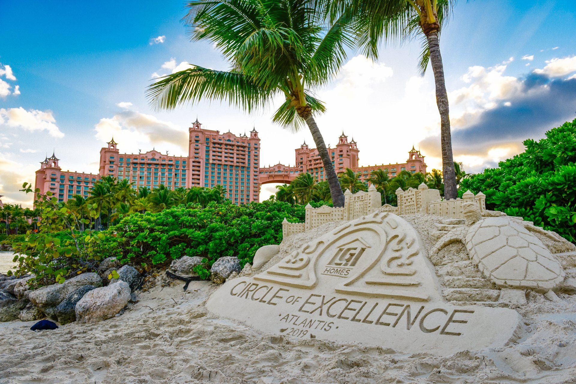 There is a sand sculpture on the beach in front of a building.