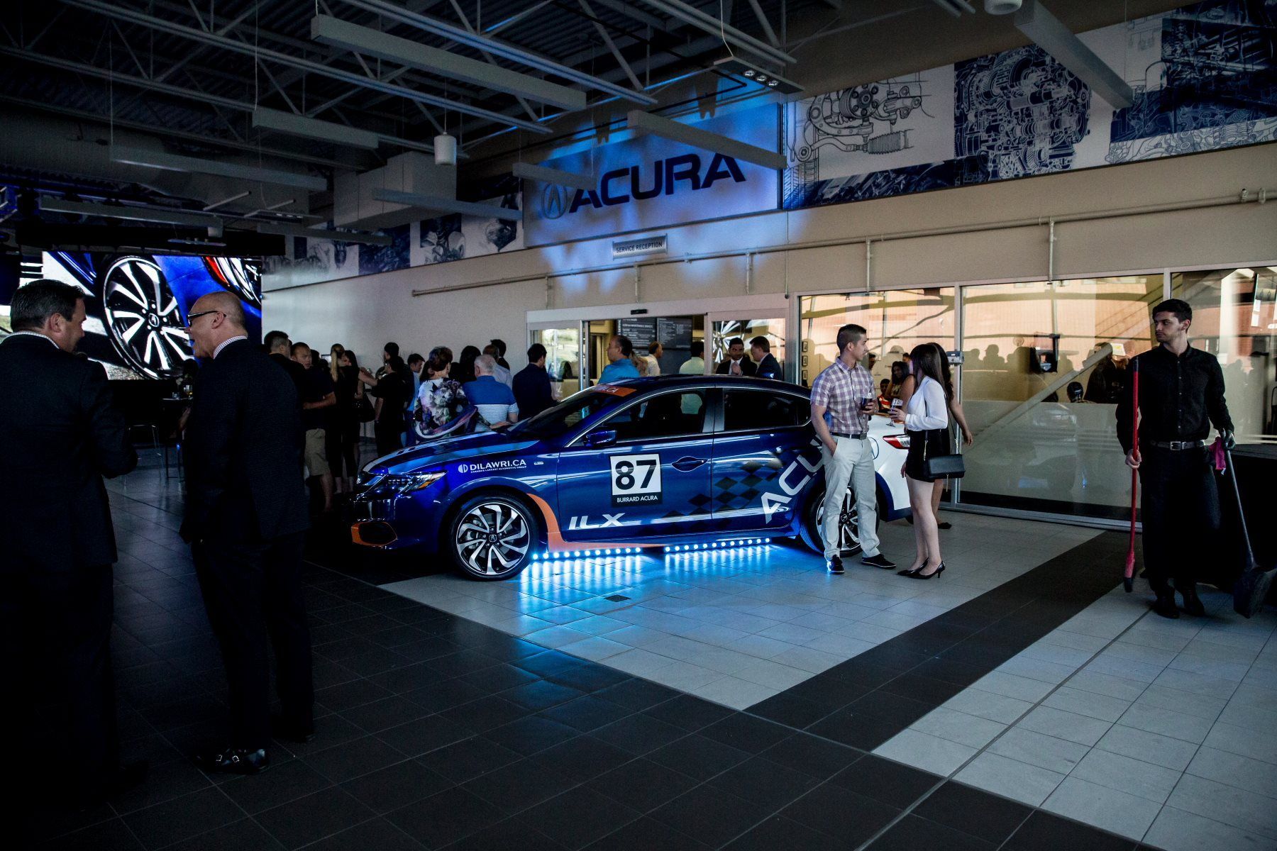 A group of people are standing around a blue car in a showroom.