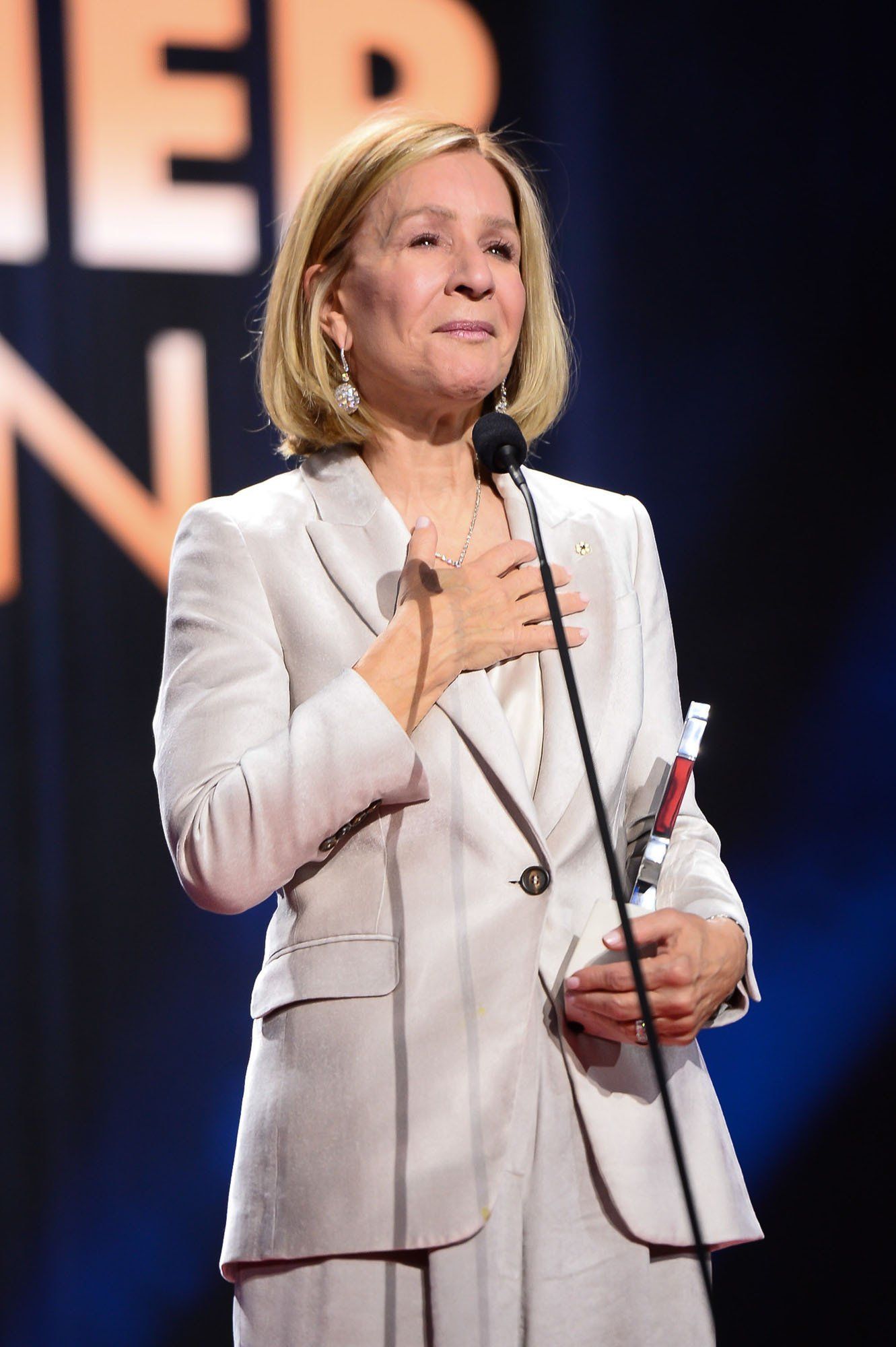 A woman in a white suit is speaking into a microphone