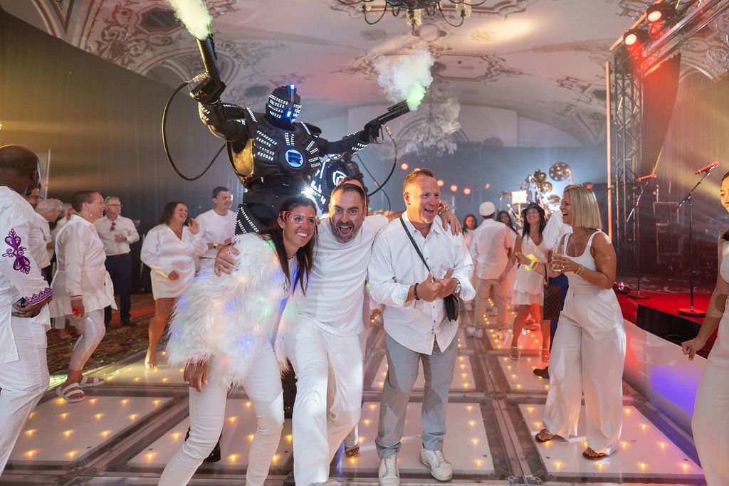 People in white outfits at a party, robot, fog, and sparkling dance floor.
