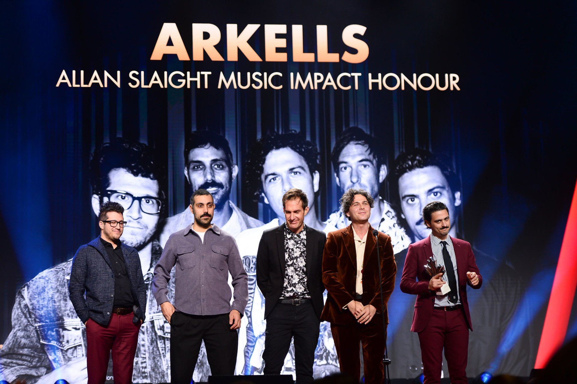 A group of men standing on a stage in front of a sign that says arkells allan slight music impact honour