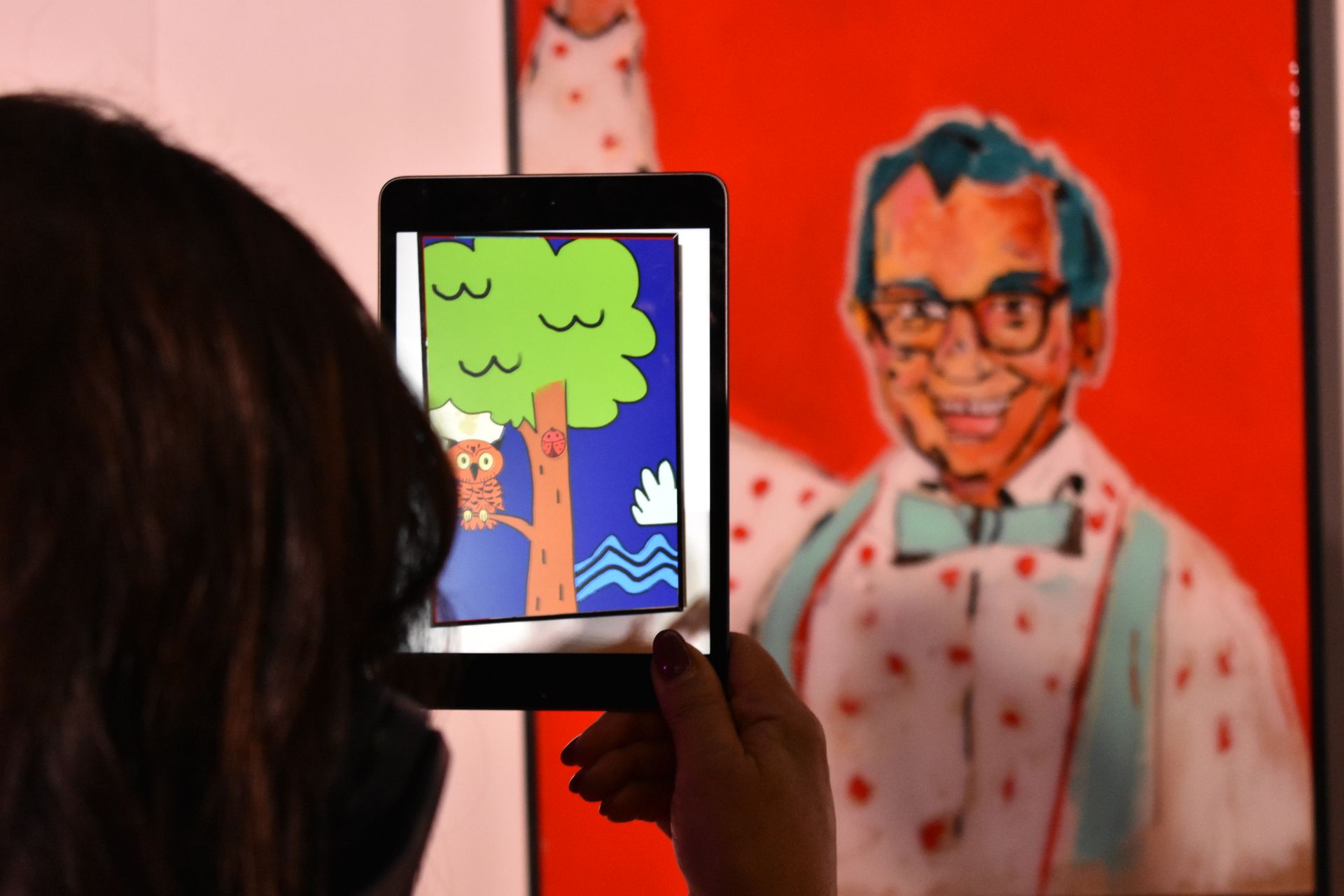 A woman is taking a picture of a cartoon on a tablet.