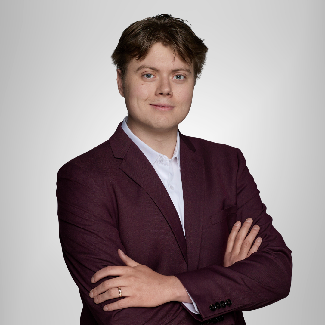 Person in a burgundy blazer with arms crossed against a light gray background
