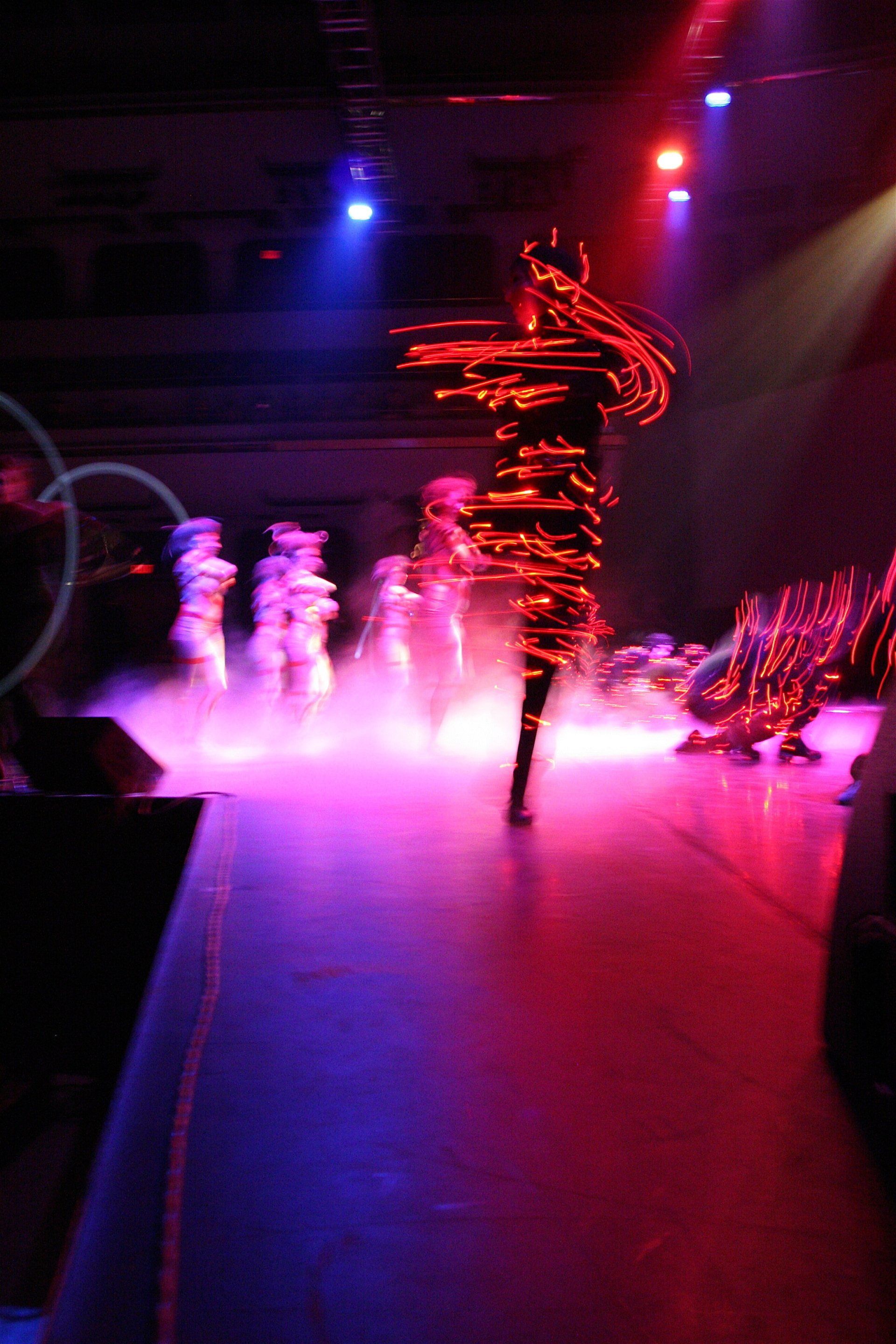 A group of people are dancing on a stage in a dark room.