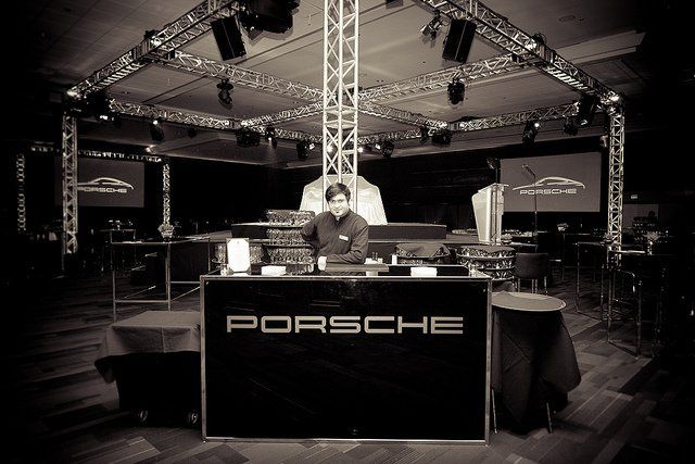 DJ at a Porsche event; black table with Porsche logo, lights and stage setup.