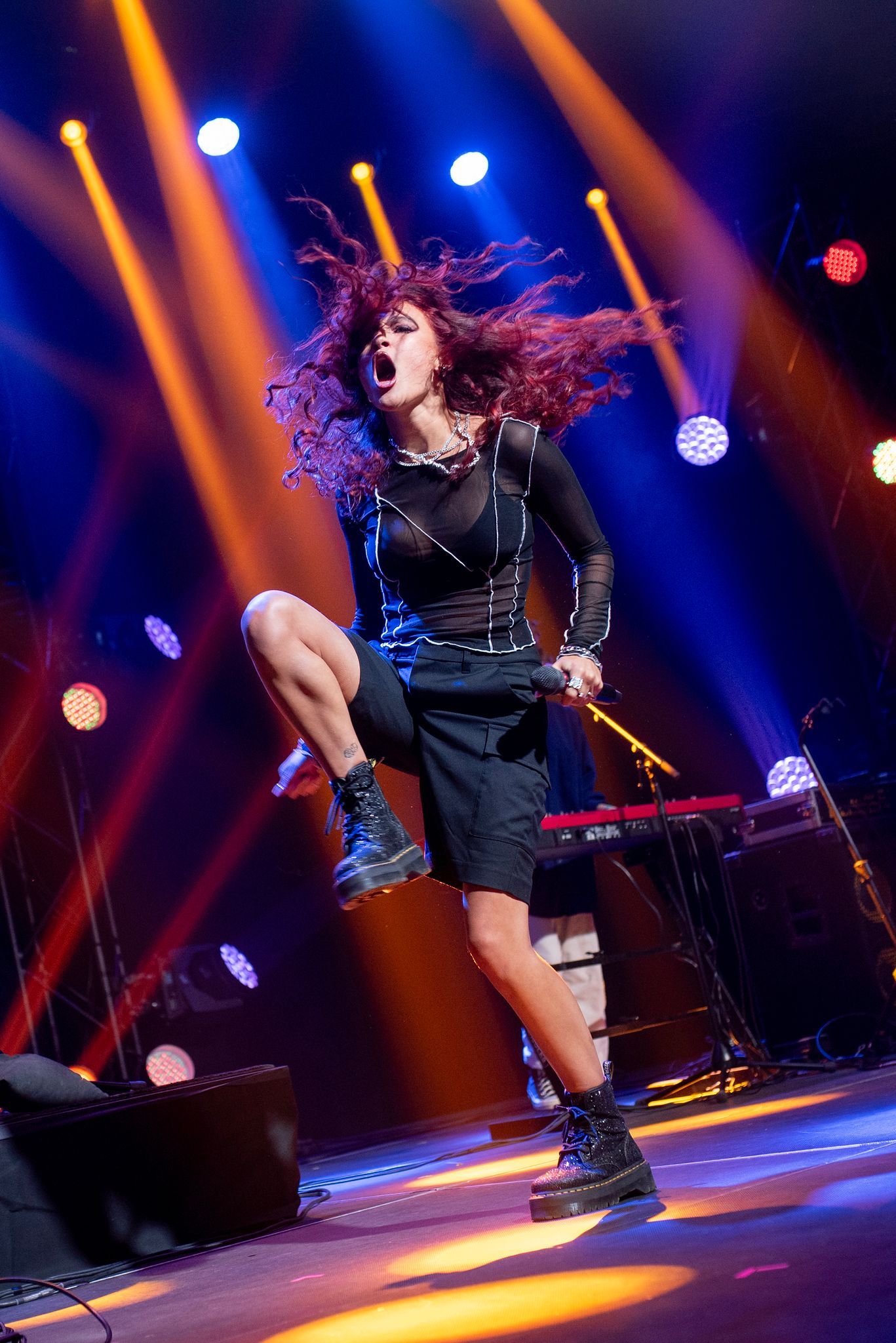 Woman performing on stage, hair flying, striking a pose, wearing black outfit, dramatic lighting.