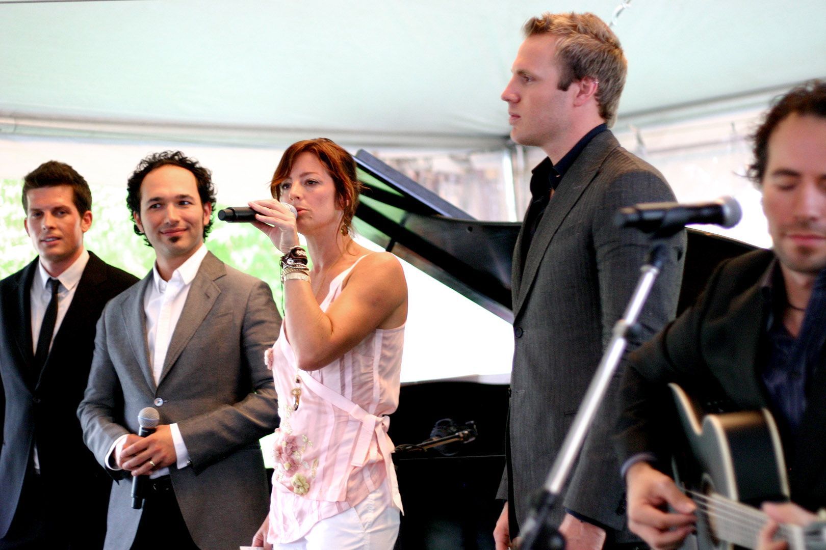 A group of men and a woman singing into microphones