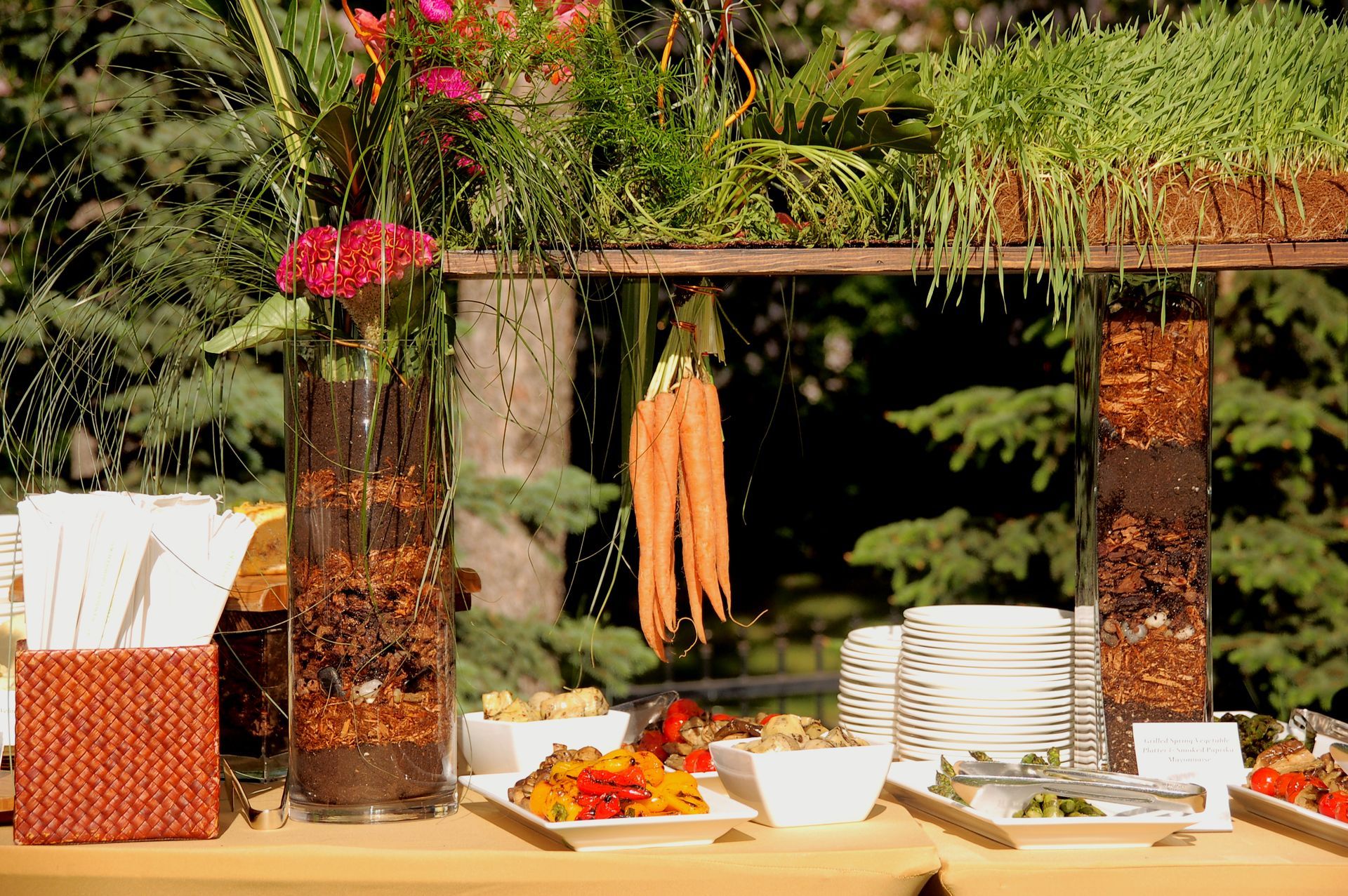 A buffet table with carrots hanging from the ceiling and plates on it.