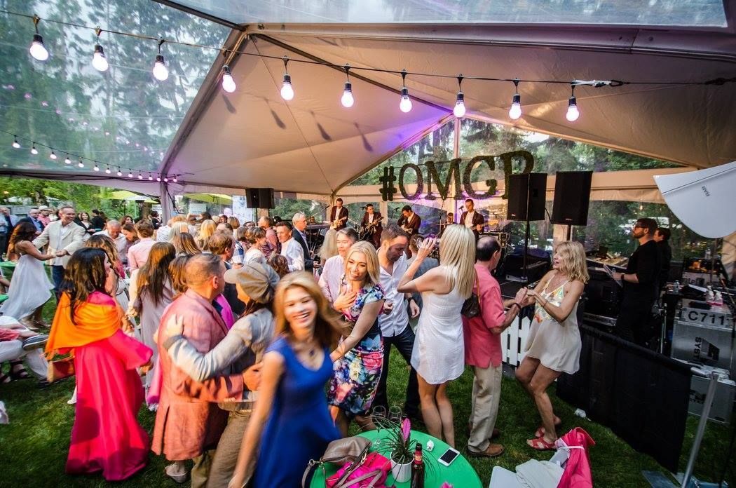 A large group of people are dancing under a tent at a party.