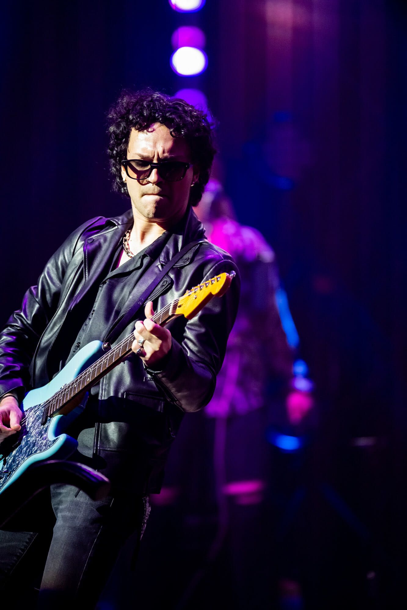 A man is playing a guitar on a stage in a dark room.