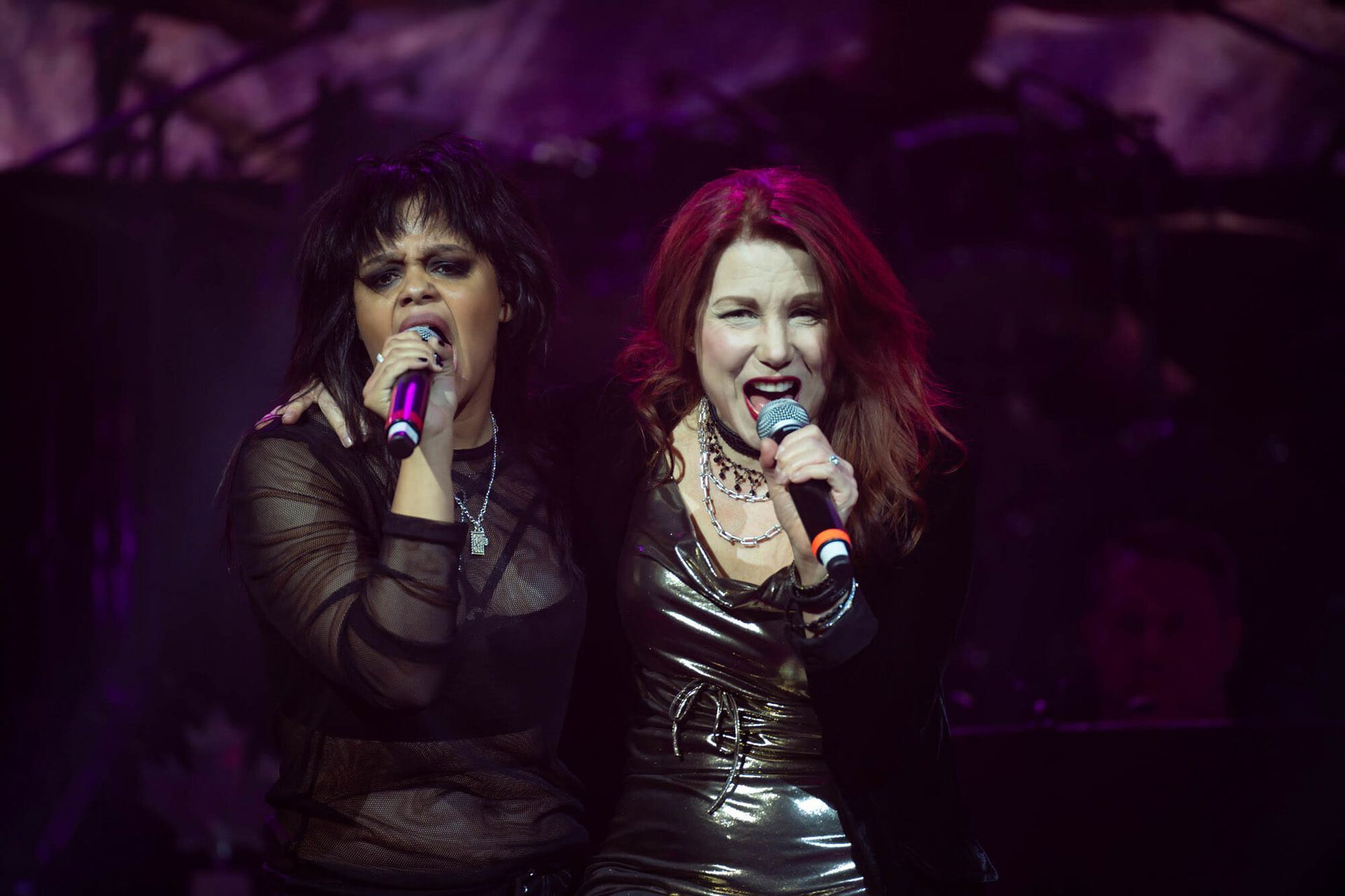 Two women are singing into microphones on a stage.