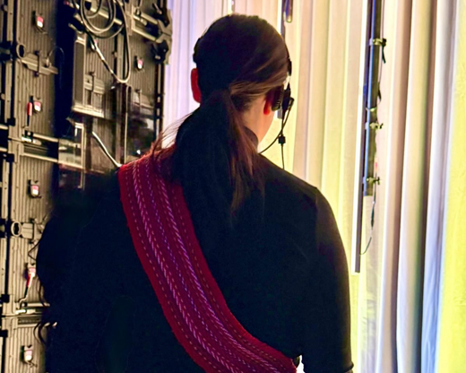 Person seen from behind near equipment, wearing a black top and pink sash by a bright doorway.