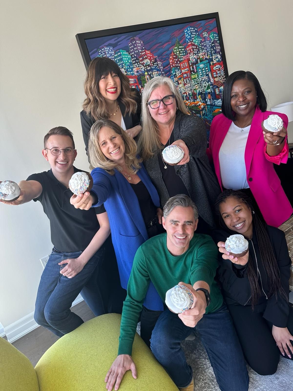 A group of people are posing for a picture while holding cupcakes in their hands.