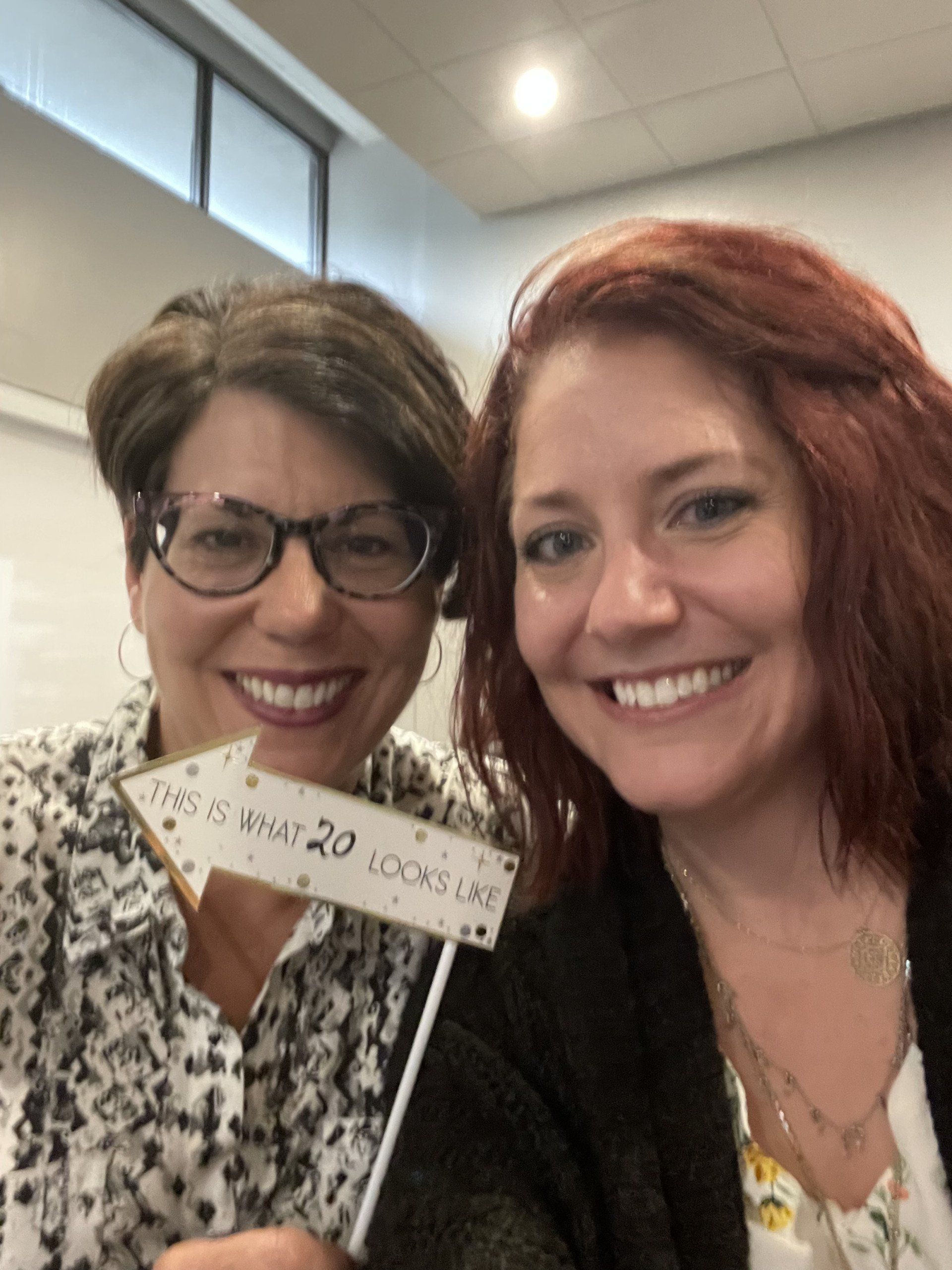 Two women are posing for a picture while holding a sign that says 