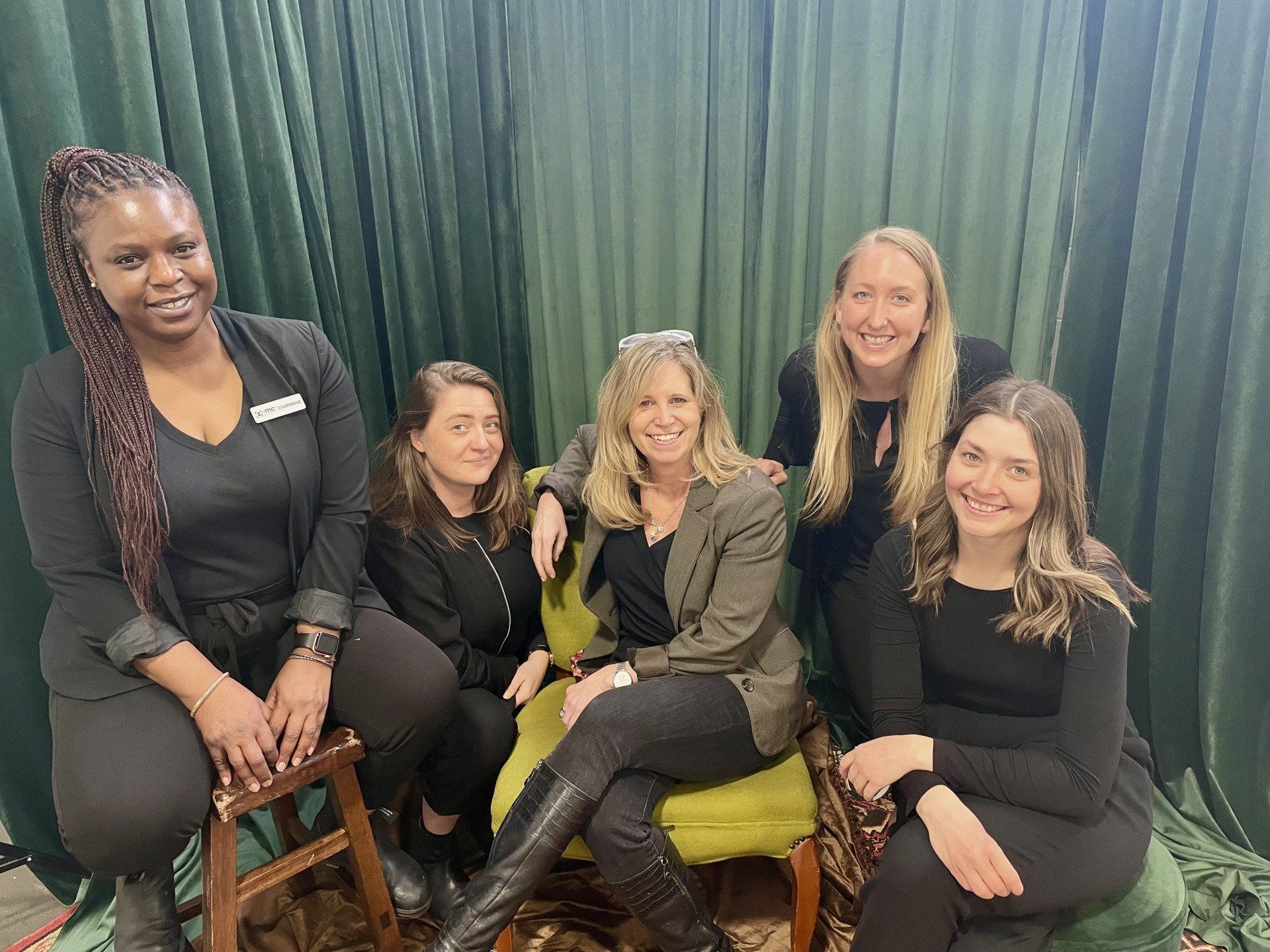 A group of women are sitting in chairs in front of a green curtain.