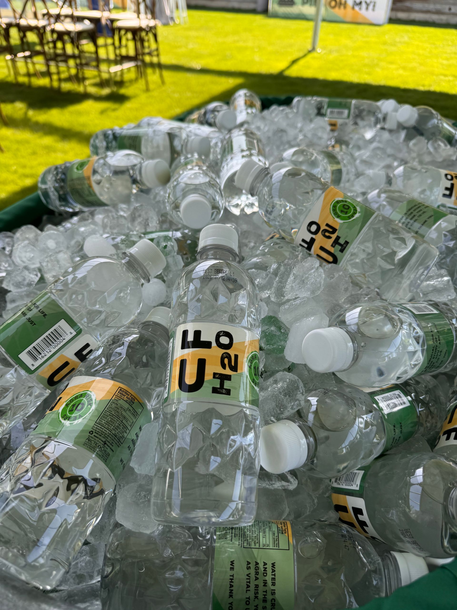 Bottled water in a cooler filled with ice. Bottles have green and white labels, some with the letters