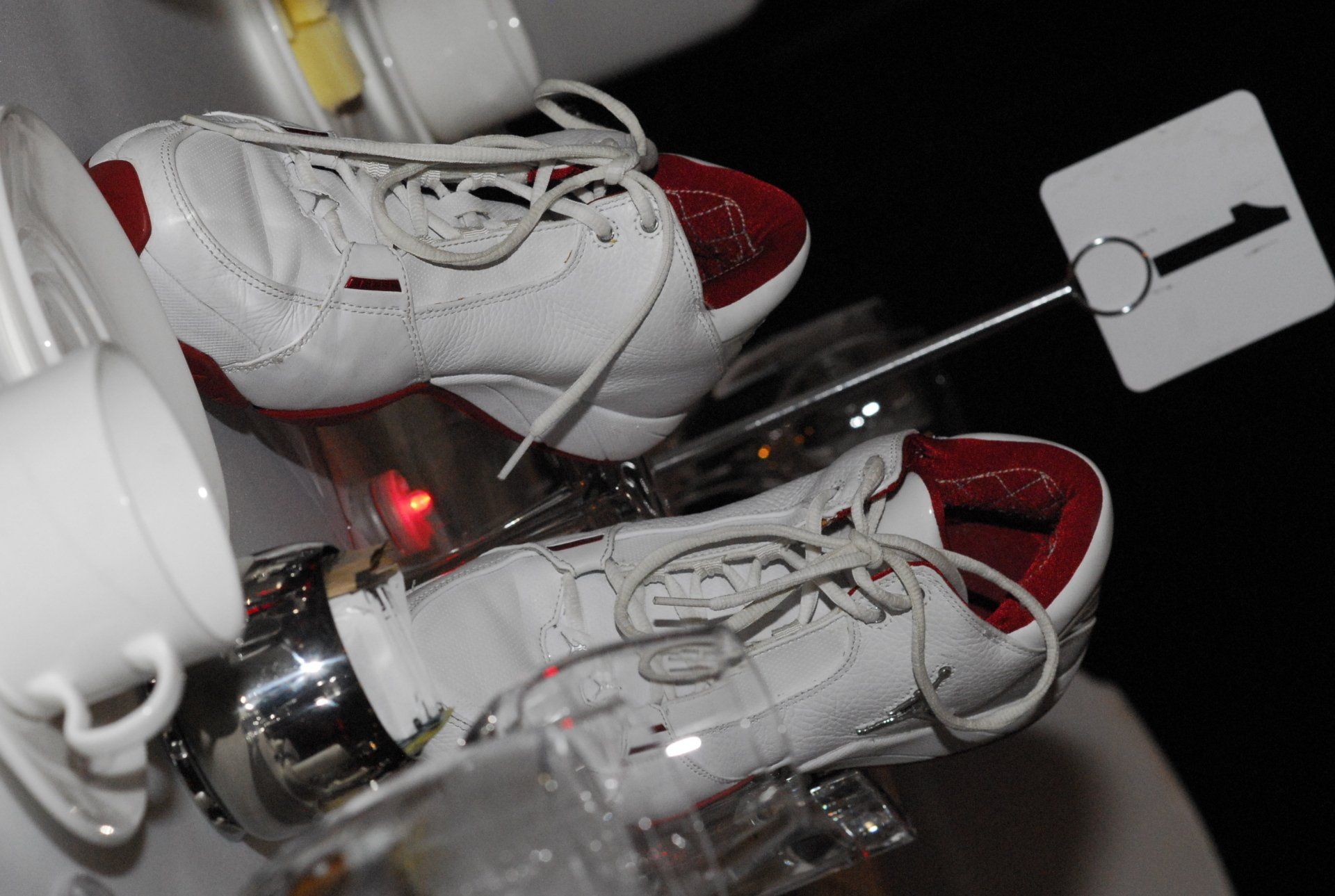 White and red sneakers atop a chrome structure, possibly art. A small sign with the number 1 is attached.
