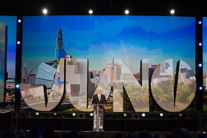 A man is giving a speech on a stage in front of a large screen that says juno.