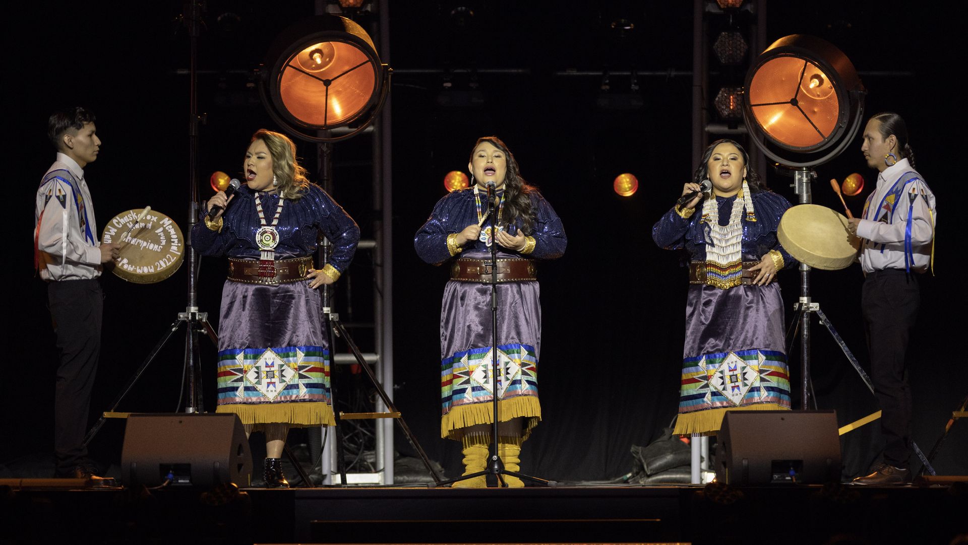 A group of people are singing and playing drums on a stage.
