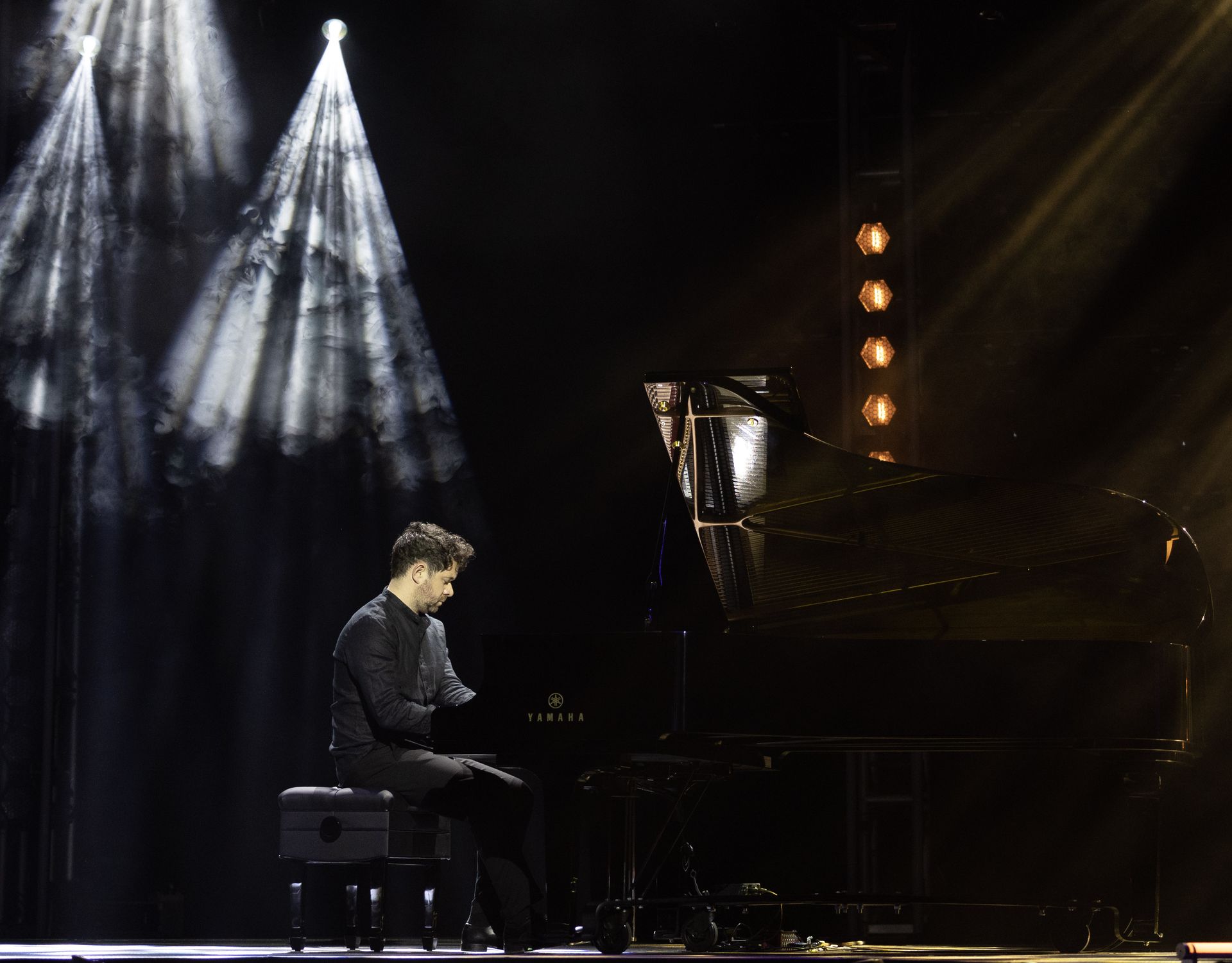 A man is playing a piano on a stage in a dark room.