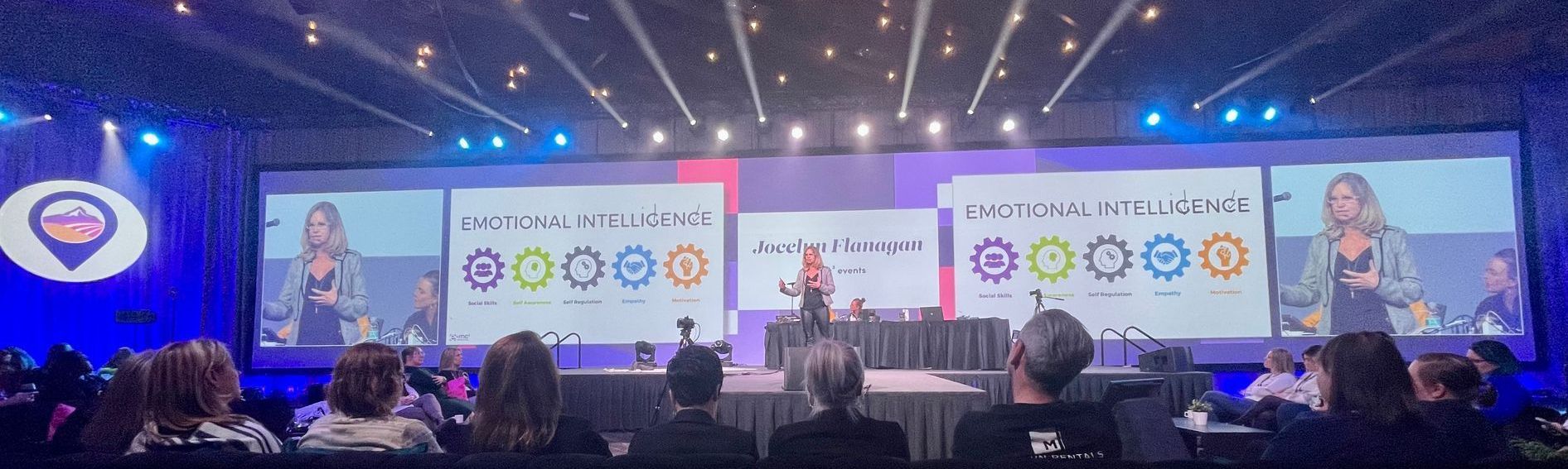 A group of people are sitting in front of a large screen at a conference.
