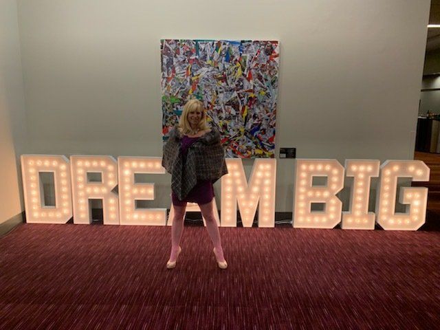 A woman stands in front of a sign that says dream big