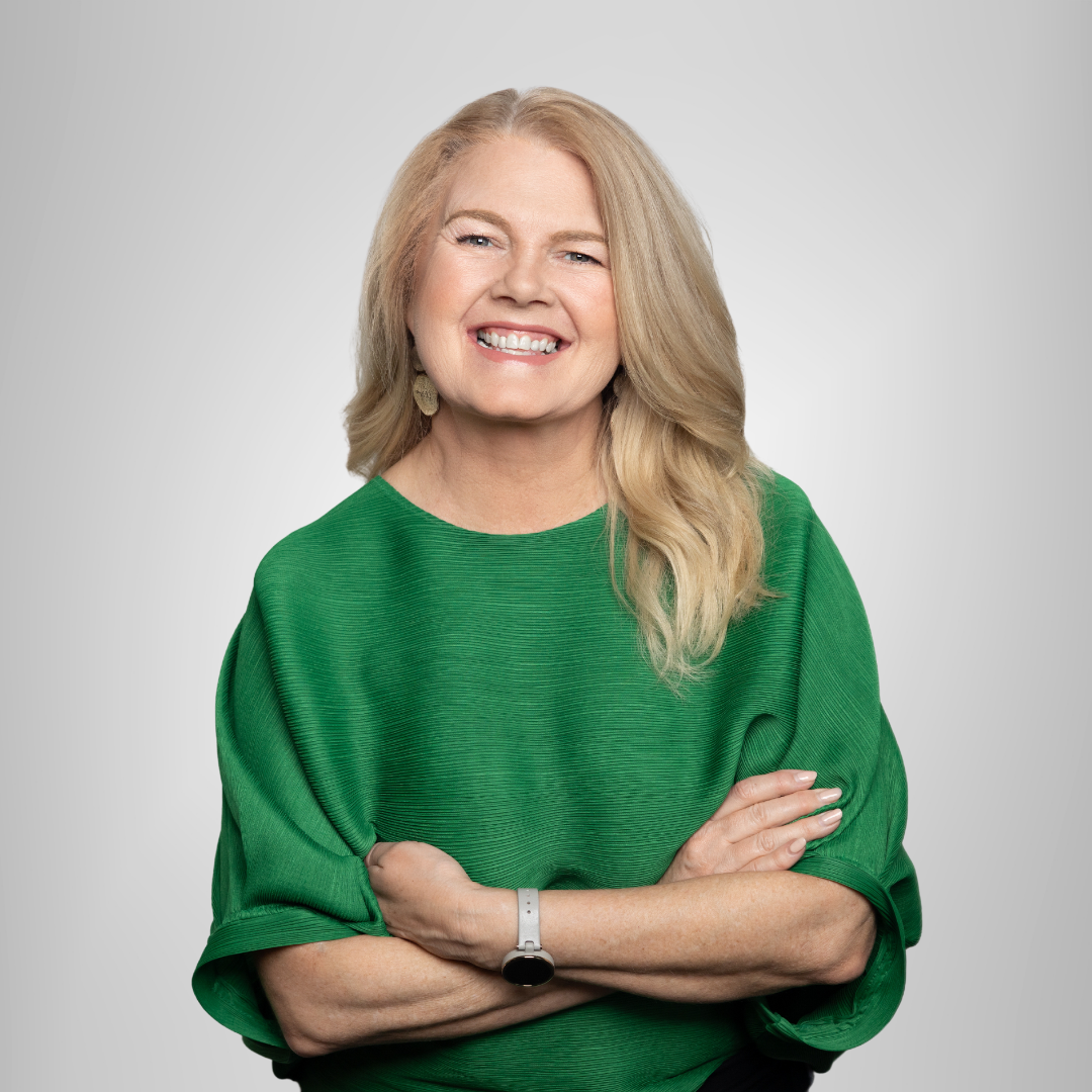 Smiling woman in a green top with arms crossed against a light gray background