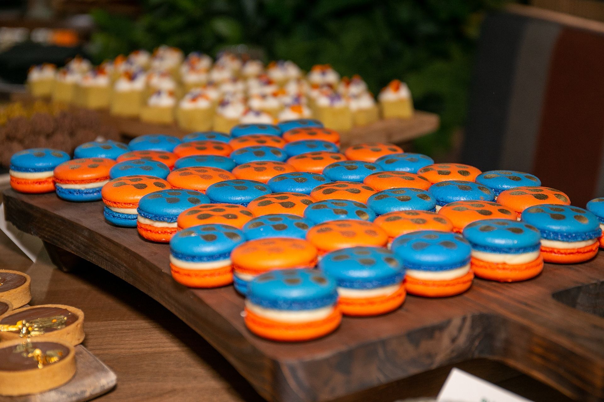 A wooden tray filled with blue and orange macarons on a table.