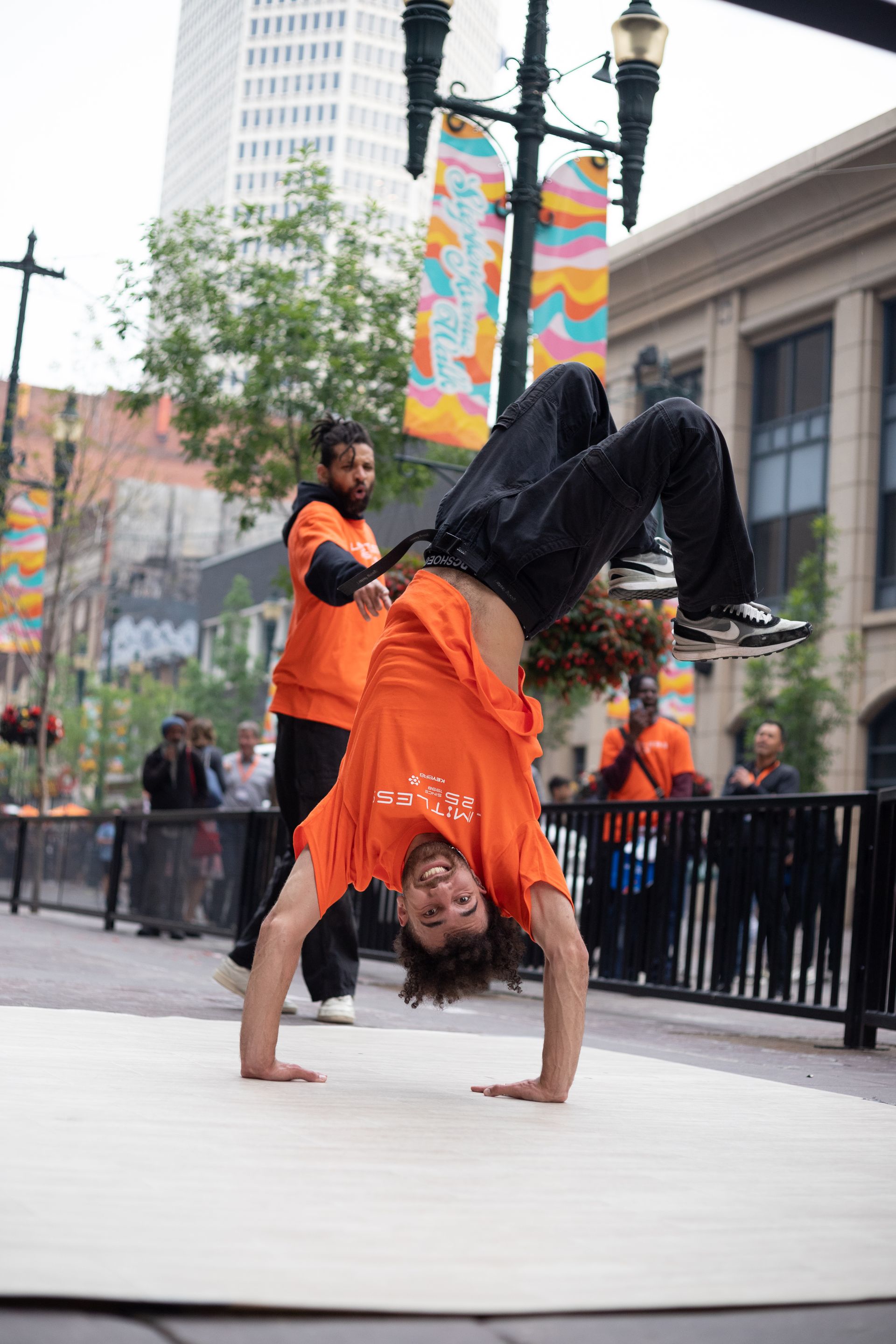 A man in an orange shirt is doing a handstand on the street.