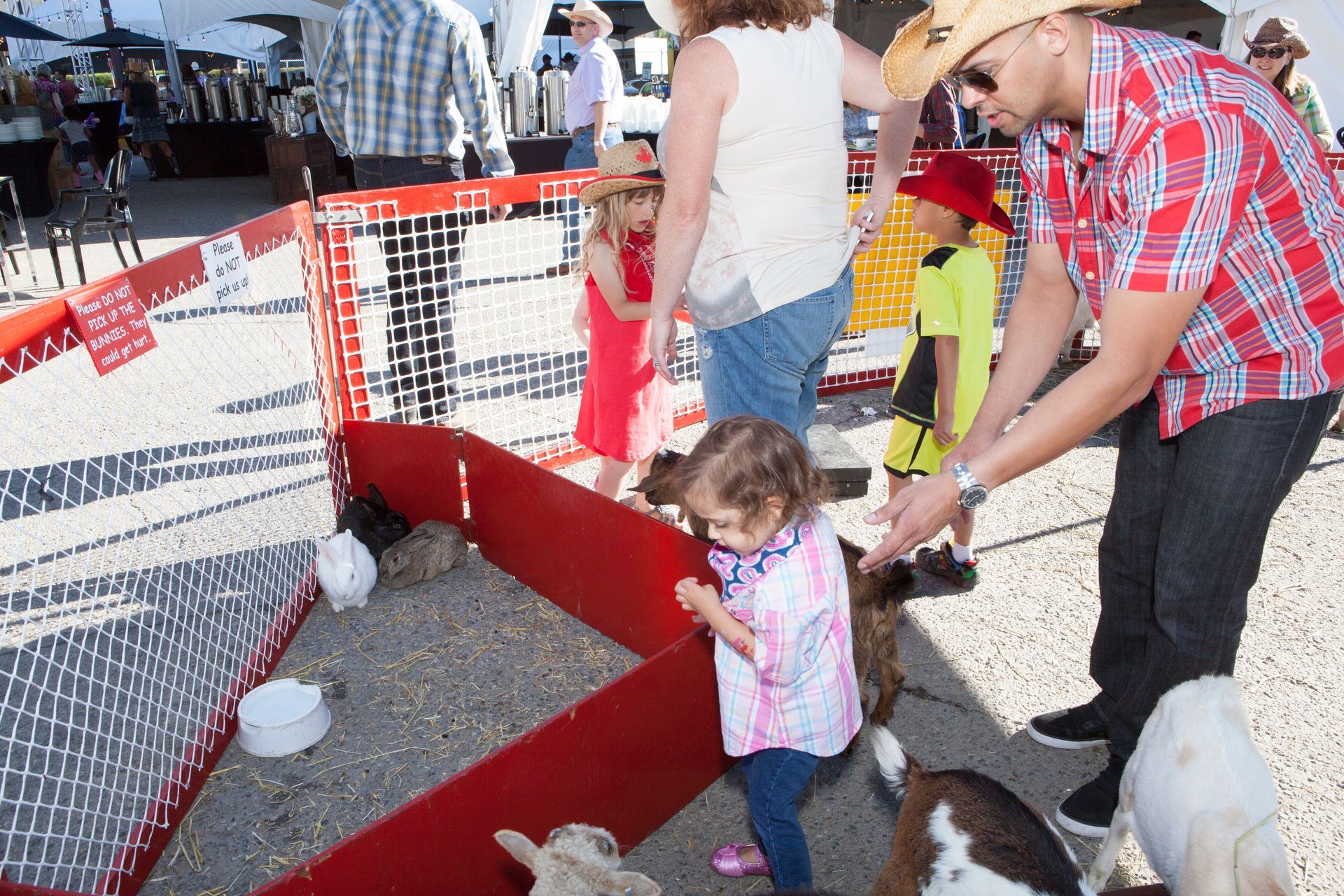 A man in a cowboy hat is feeding a little girl a goat