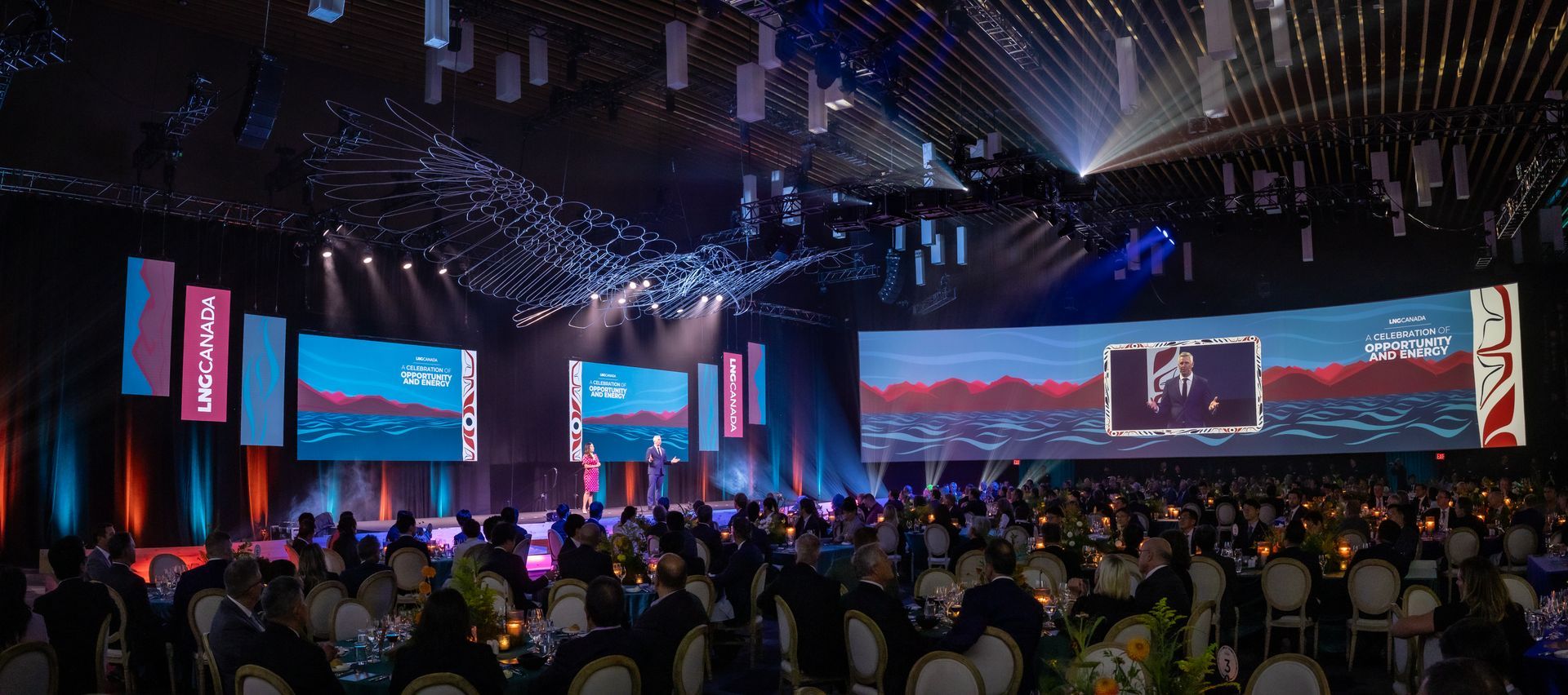 Crowded indoor concert with a large stage, bright screens, and blue-purple lighting