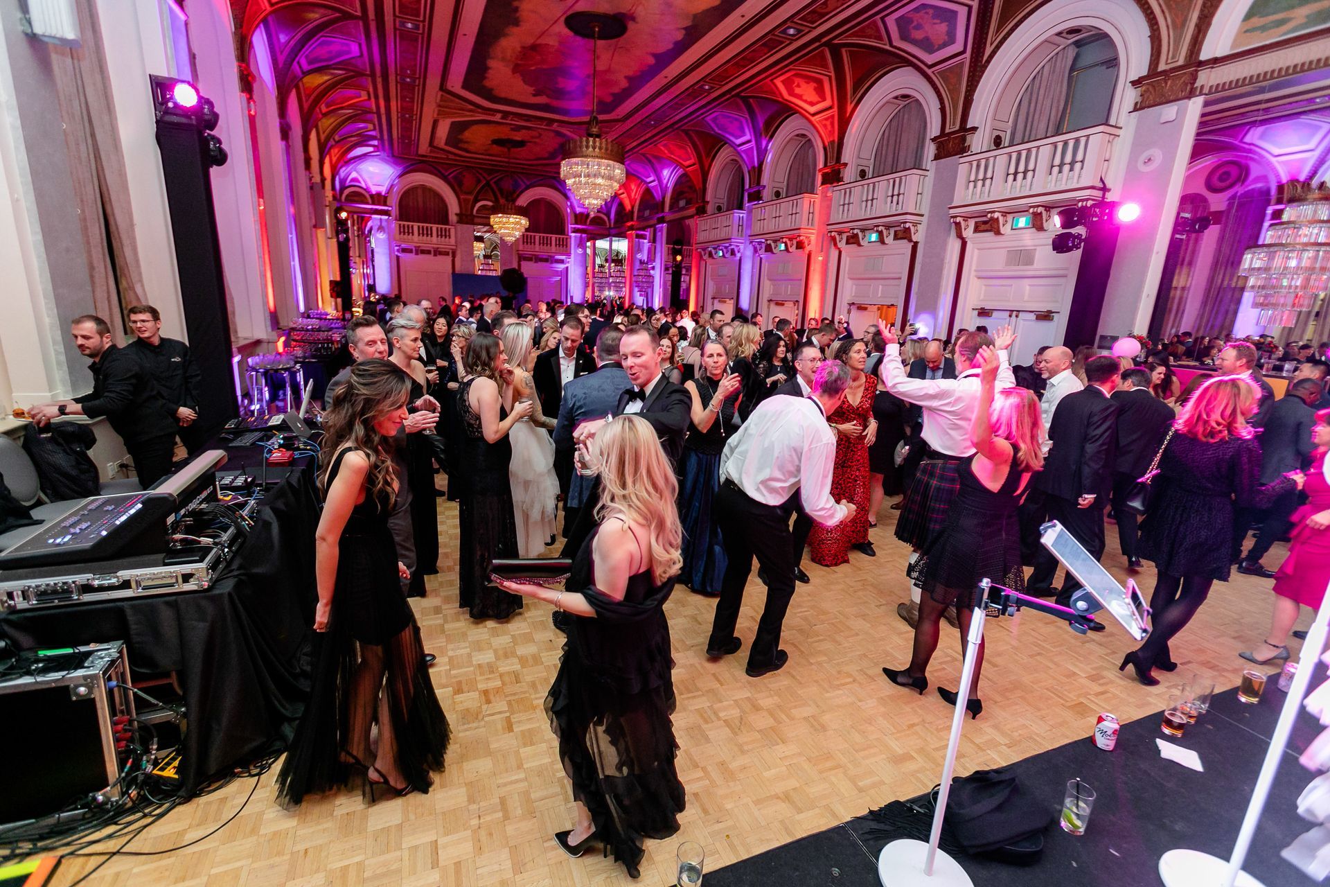 A large group of people are dancing in a large room at a party.