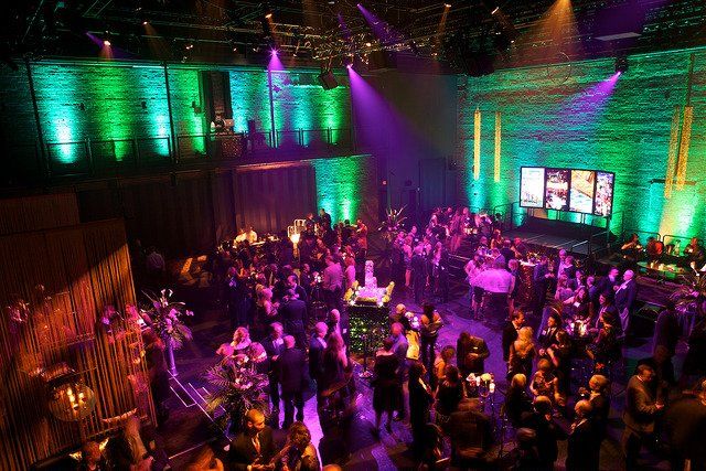 A large crowd of people are gathered in a large room with purple and green lights.