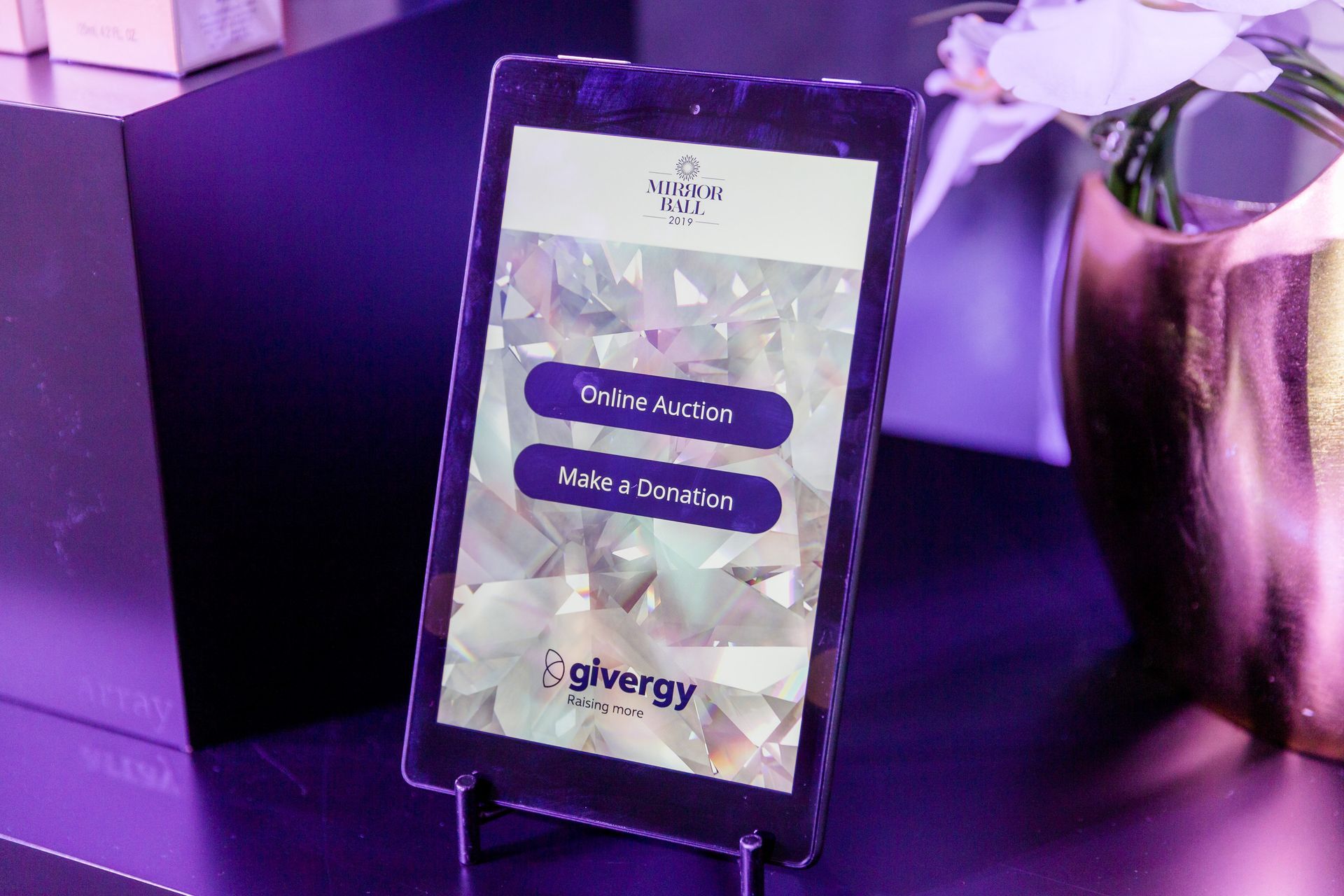 A purple tablet is sitting on a table next to a vase of flowers.