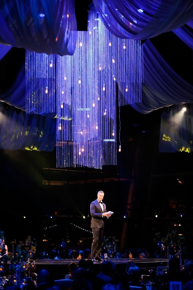 A man in a tuxedo is standing on a stage in front of a large chandelier