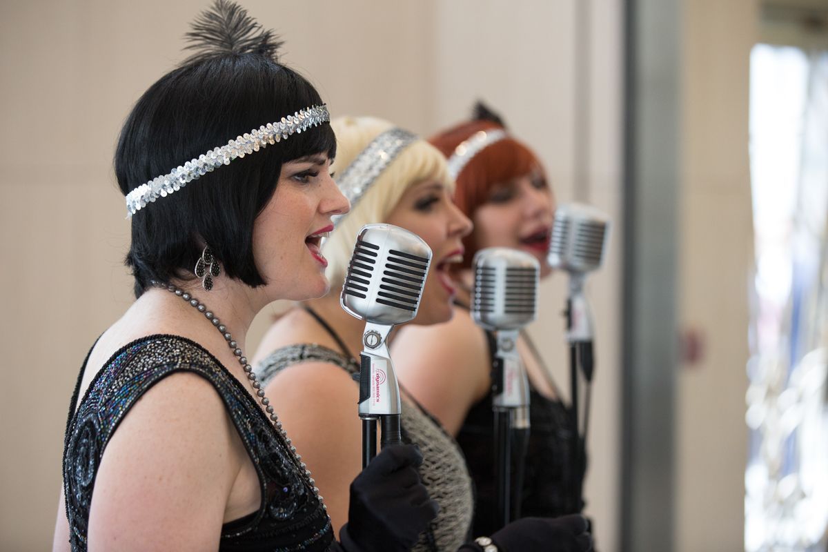 Three women are singing into microphones in a row.