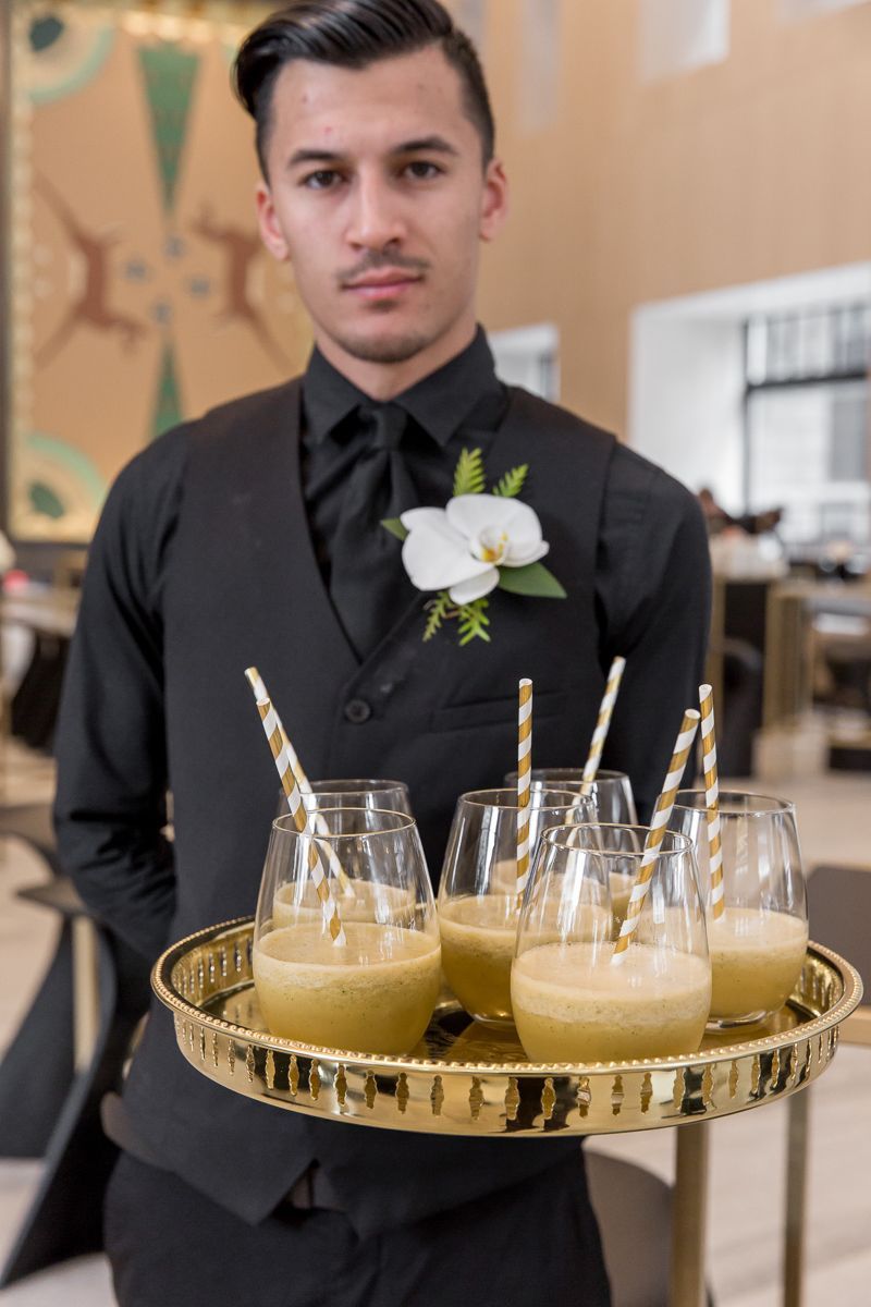 A man in a black suit is holding a tray of drinks with straws.