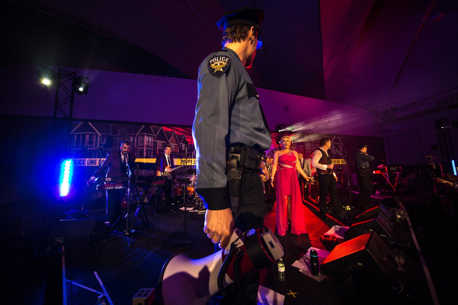 A man in a police uniform is standing in front of a crowd of people at a party.
