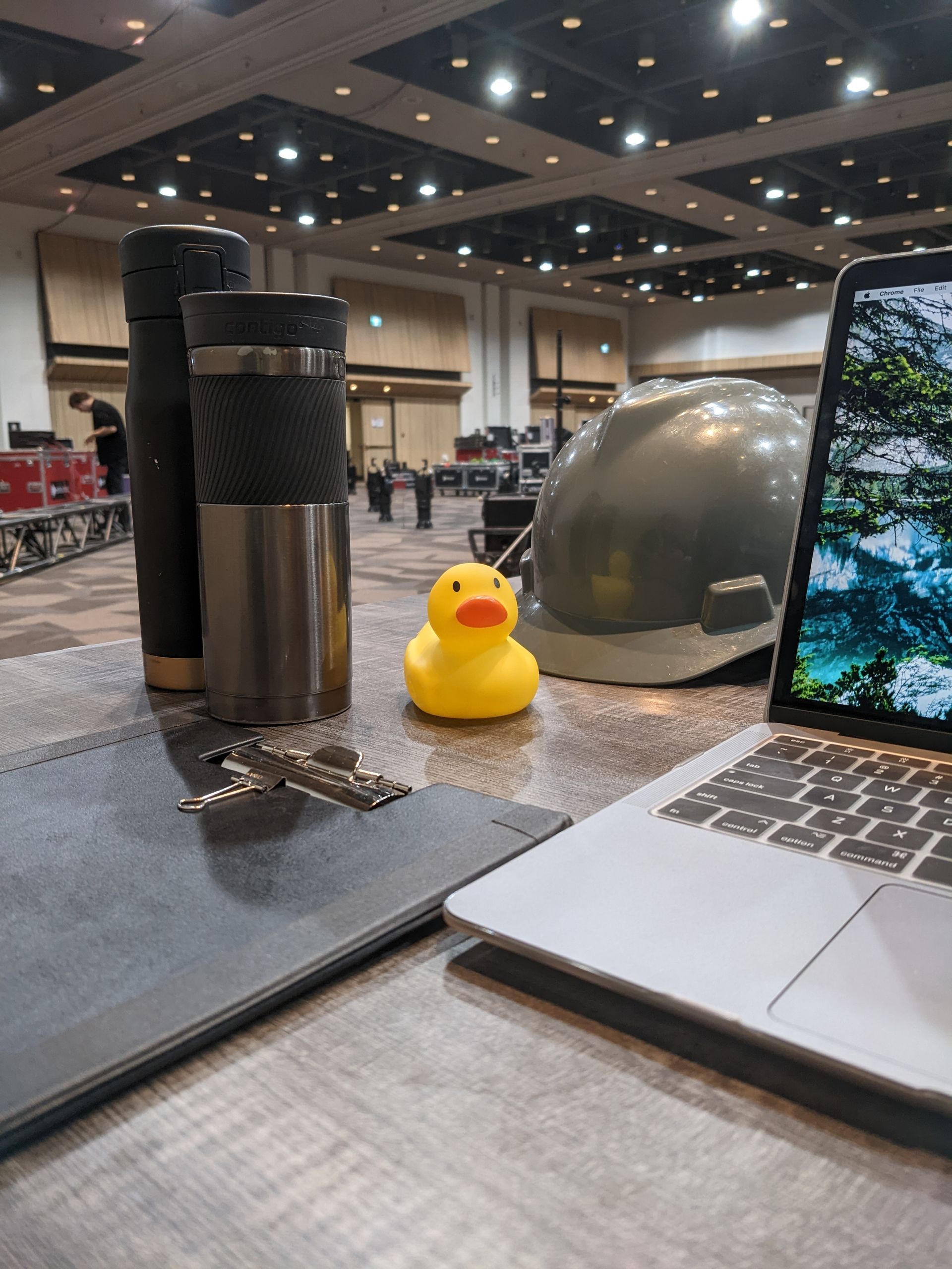 A yellow rubber duck sits on a desk next to a laptop