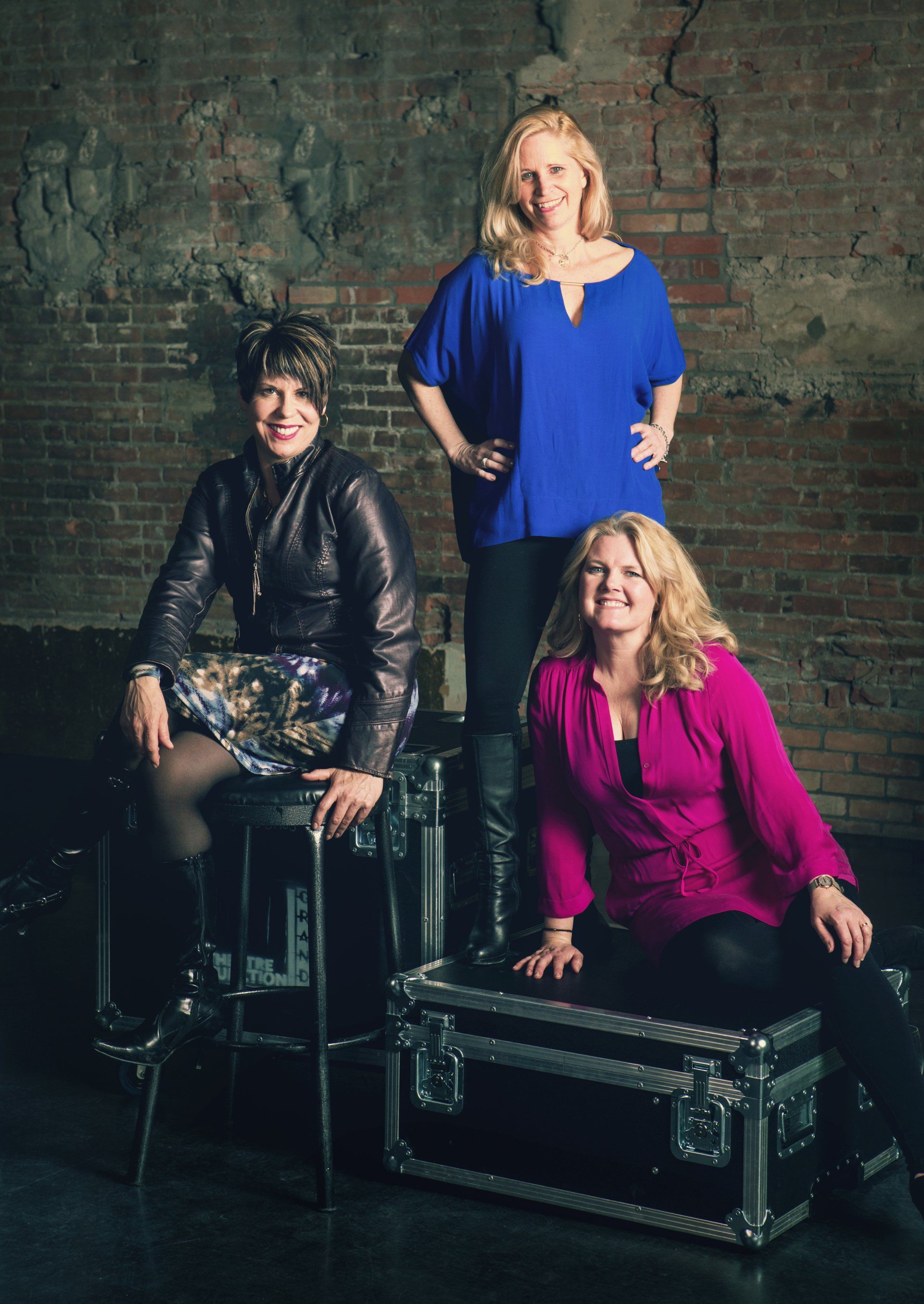 Three women are posing for a picture in front of a brick wall.