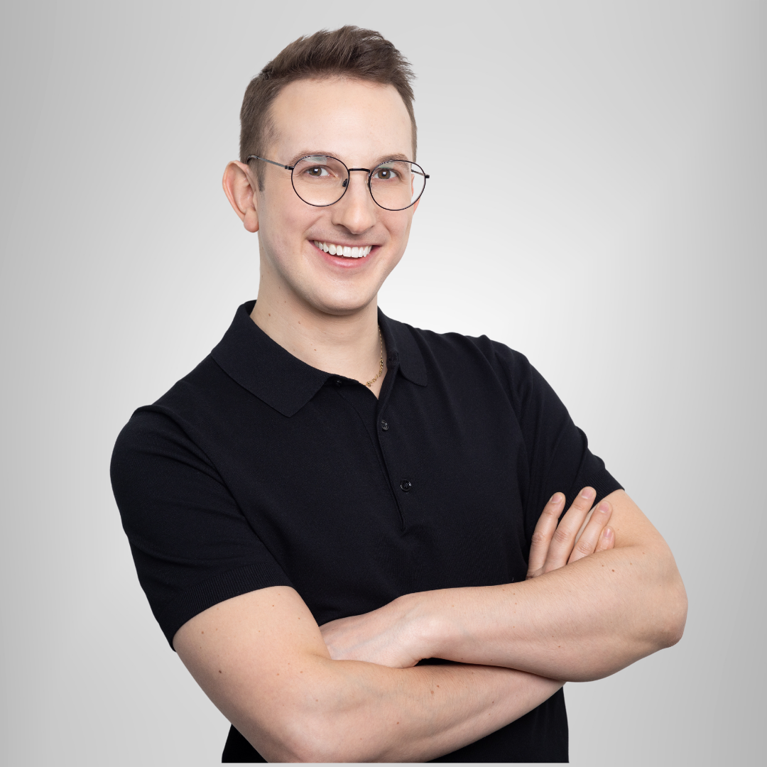 A man wearing glasses and a black shirt is smiling with his arms crossed