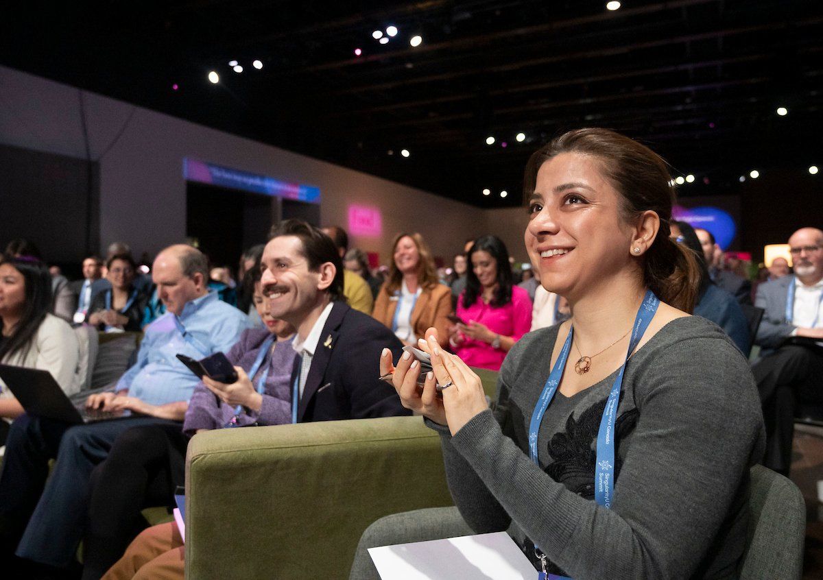 A group of people are sitting in chairs at a conference and applauding.