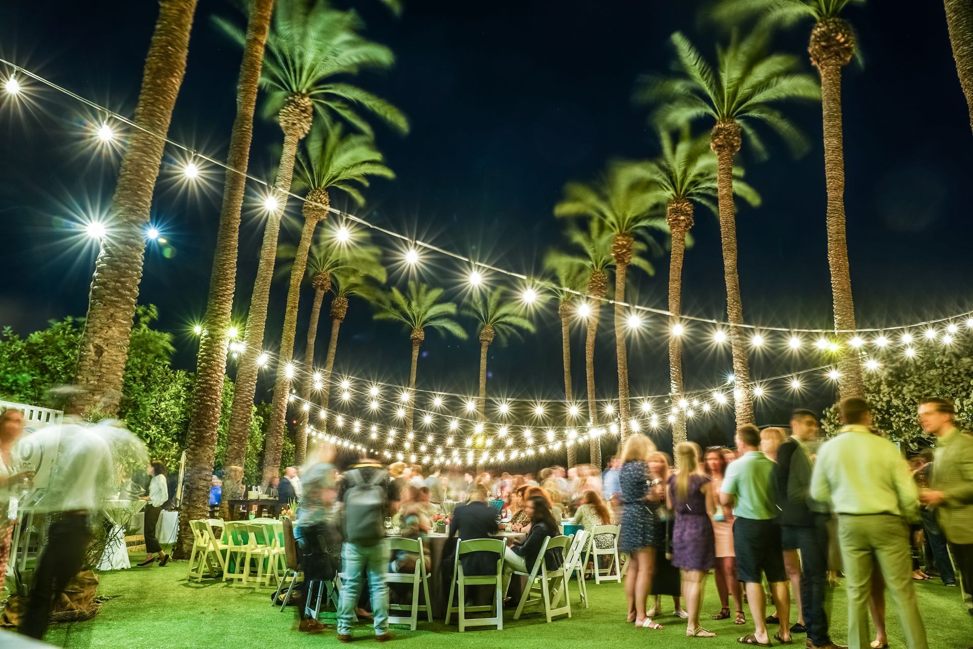 A group of people are sitting at tables under a string of lights.