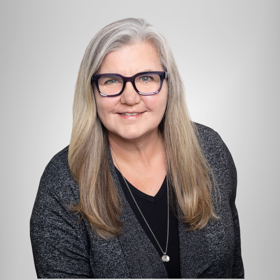A woman wearing glasses and a black sweater is smiling for the camera.